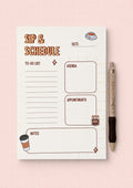 Notebook with 'Sip & Schedule' design on a pink background