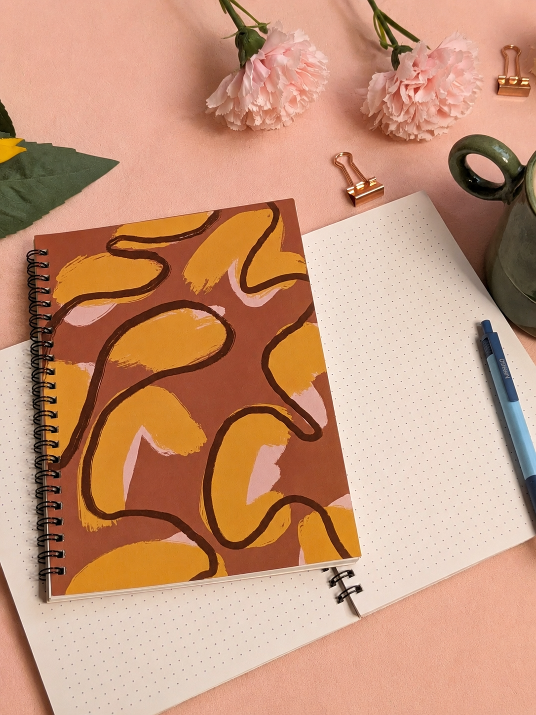 Notebook with a patterned cover on a desk with flowers and stationery items.