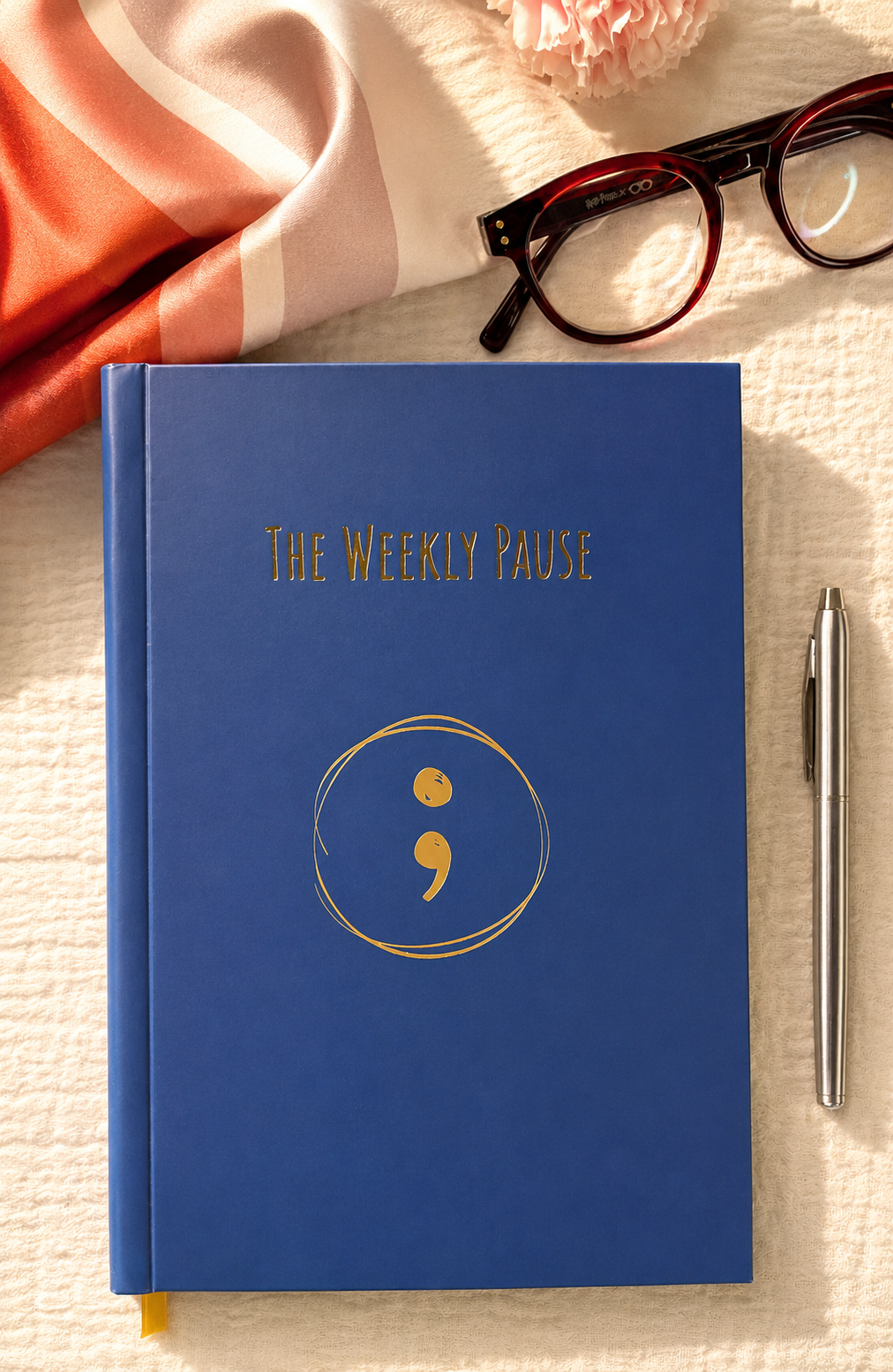 Blue notebook titled 'The Weekly Pause' with a pen and glasses on a textured surface
